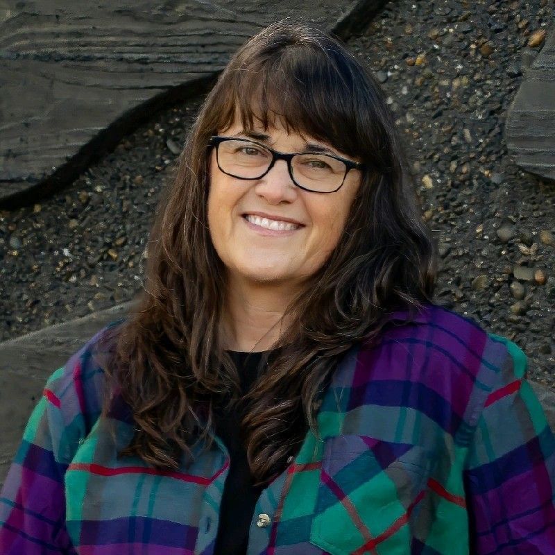A woman wearing glasses and a plaid shirt is smiling for the camera.