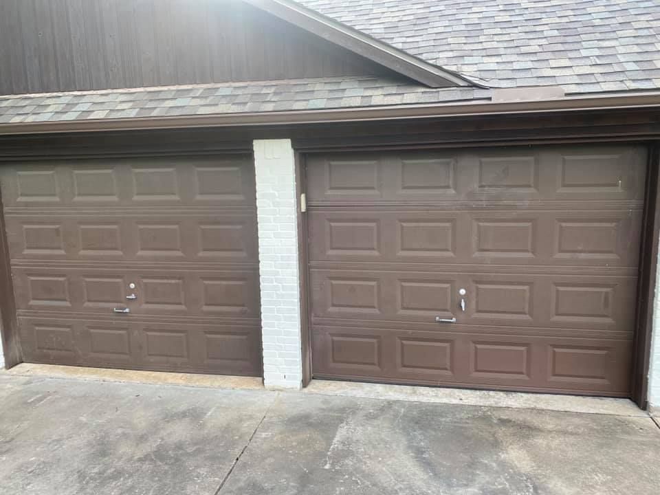 Two brown garage doors, side by side, beneath a roof, separated by a white brick pillar.