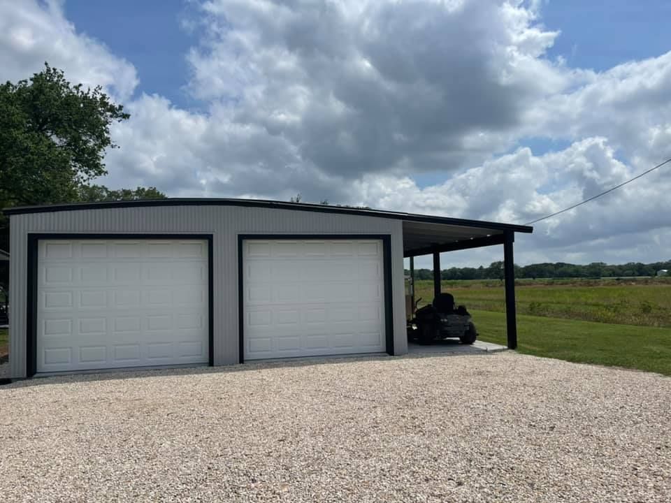Two-car gray metal garage with a carport on gravel. A riding mower is parked under the carport; cloudy sky.