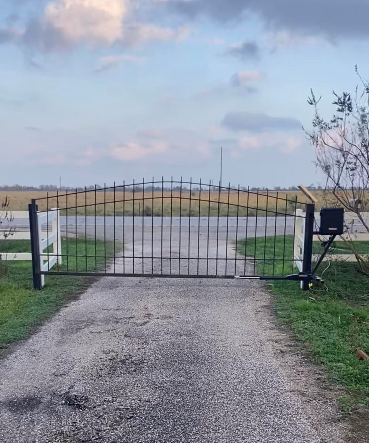 Gravel driveway leads to a closed black wrought-iron gate with an automatic opener.
