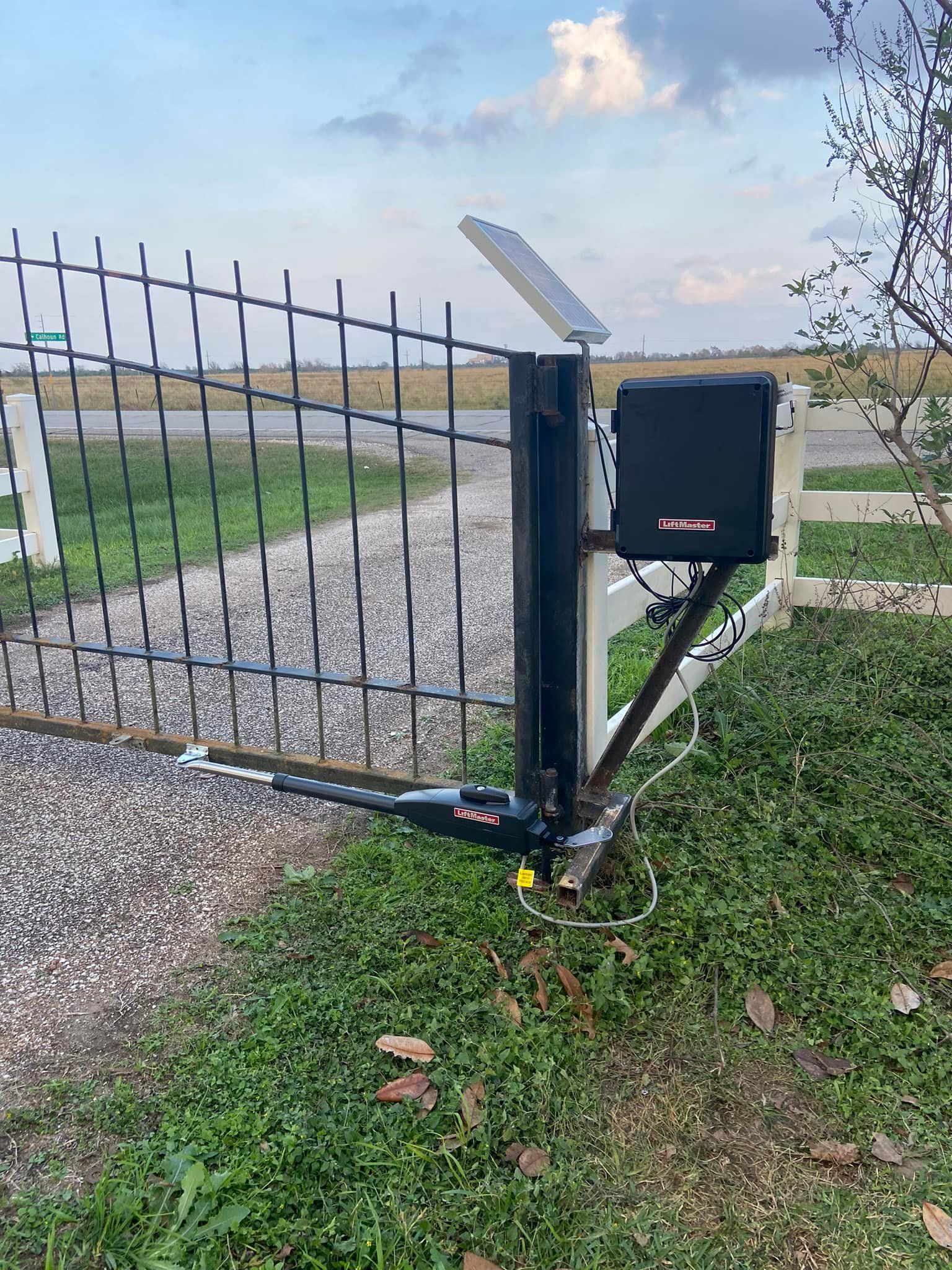Black automatic gate with solar panel and control box, mounted on a fence post.