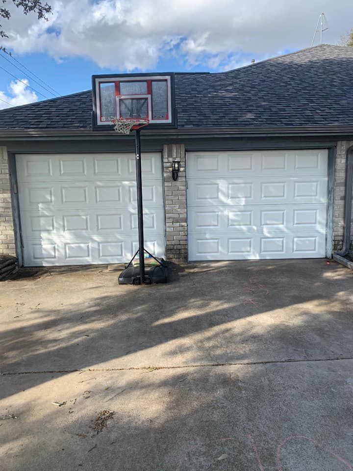 Two white garage doors with a basketball hoop in front, under a roof.