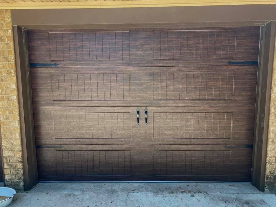 Brown wooden garage door with decorative panels, black hardware, and two handles.