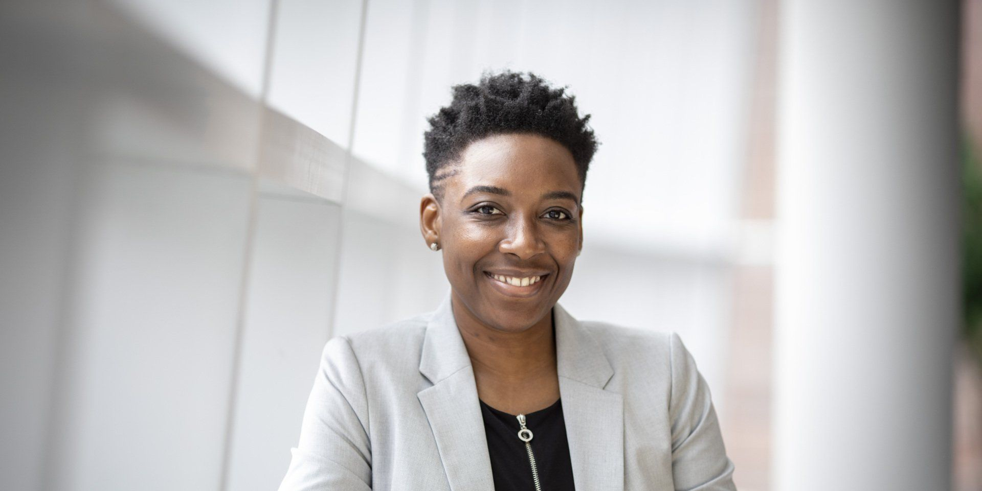 Smiling person in a light gray blazer standing in a bright office setting