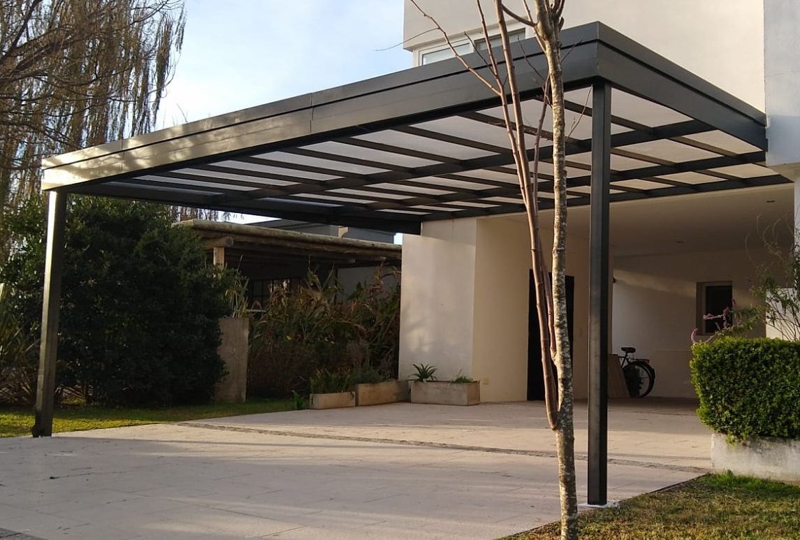 Cochera con marco negro y techo translúcido, adosada a una casa moderna de color blanco.