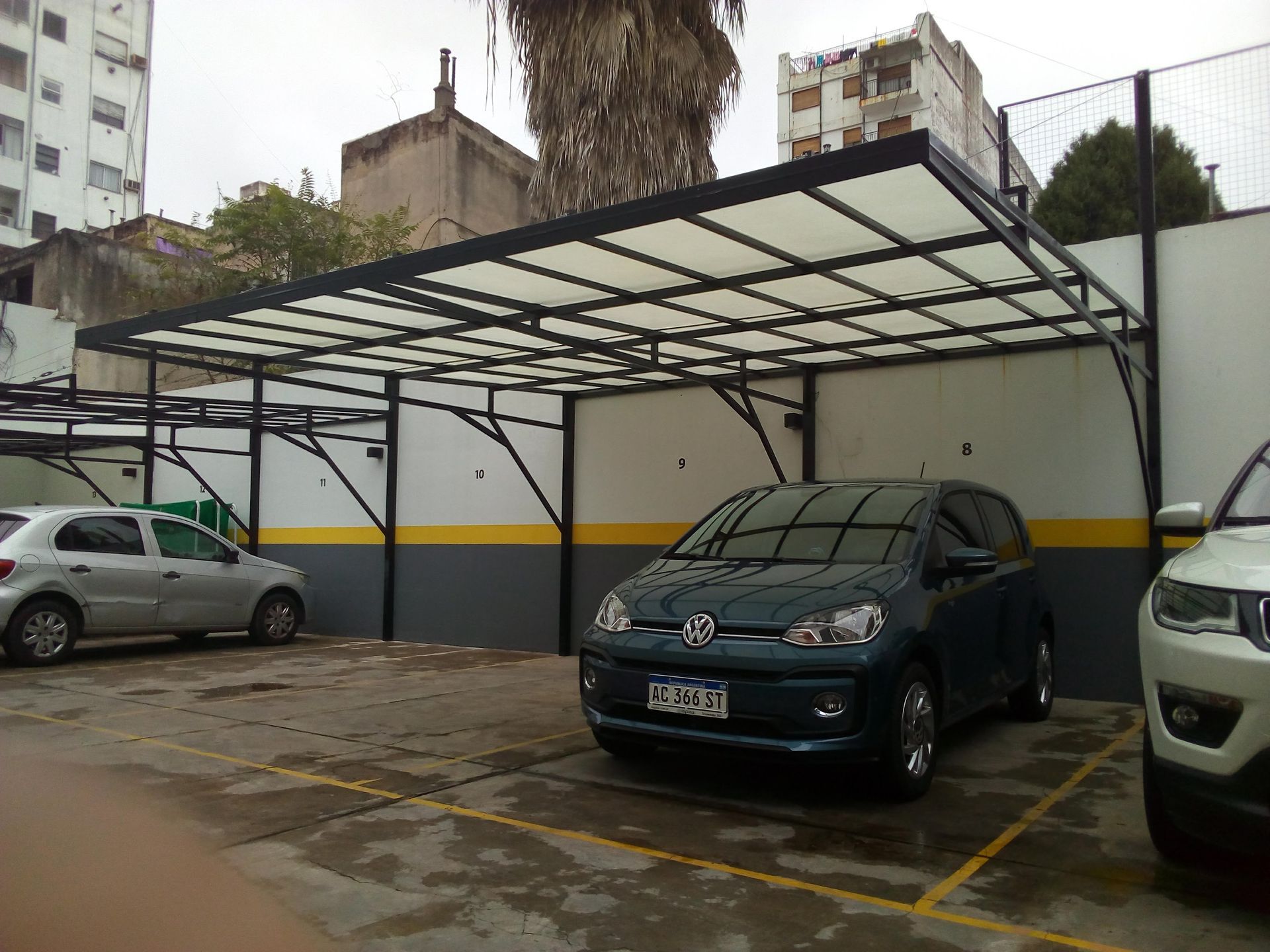 Un techo de cochera de edificio resistente al granizo protejiendo un coche azul.