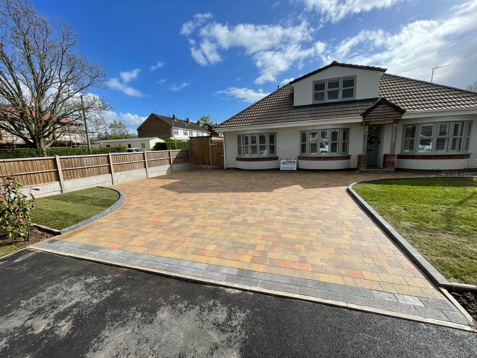 Multi-tone block paving drive with a charcoal border and curved lawn edges in front of a white bungalow in Binley Woods