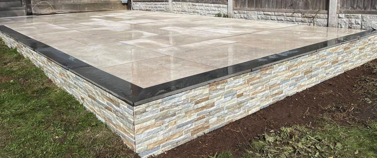 Corner of the raised porcelain patio showing split-face cladding and anthracite copings