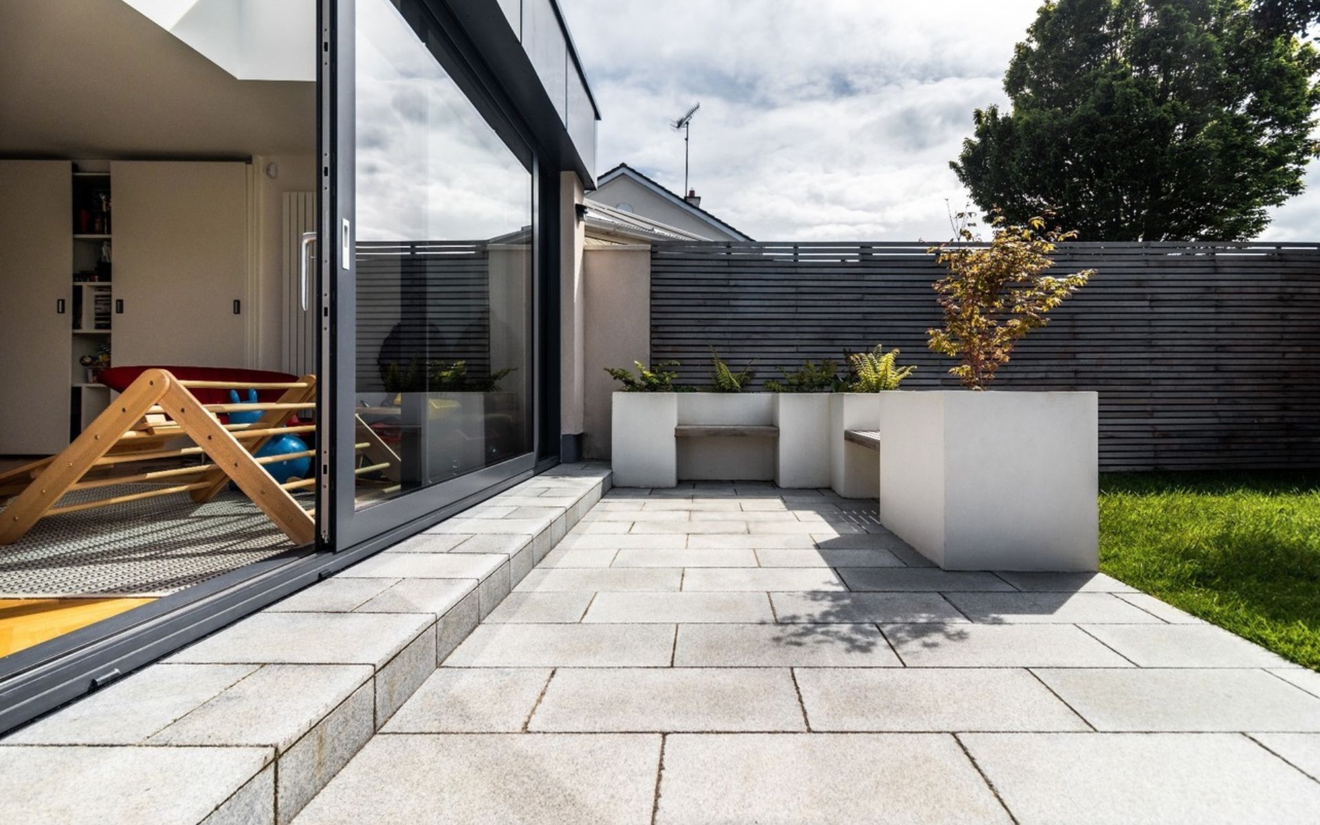 a patio with a bench and planters in front of a house