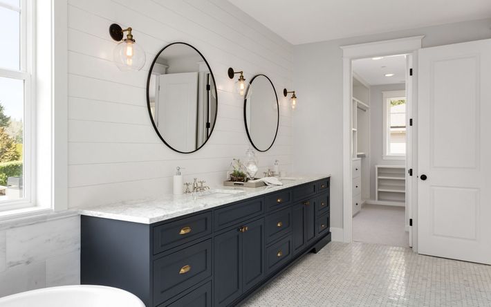 a bathroom with two sinks , two mirrors , a tub and a walk in closet .