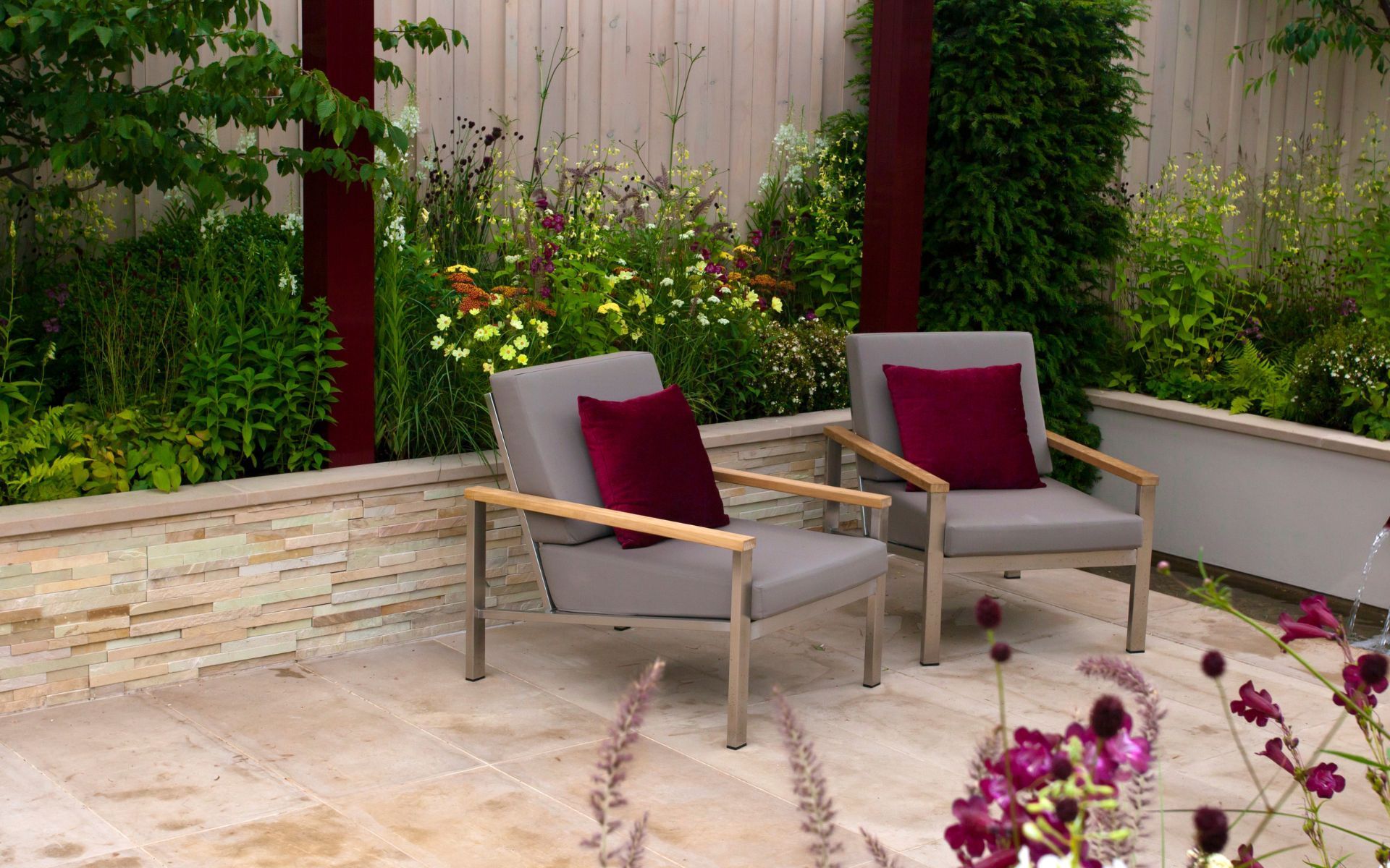 two chairs with purple pillows are sitting on a patio in a garden .