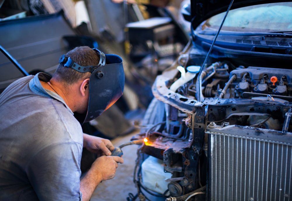A Man Wearing A Welding Mask Is Working On A Car In A Garage — Chris's Automotive & Marine Electrics In Darwin, NT