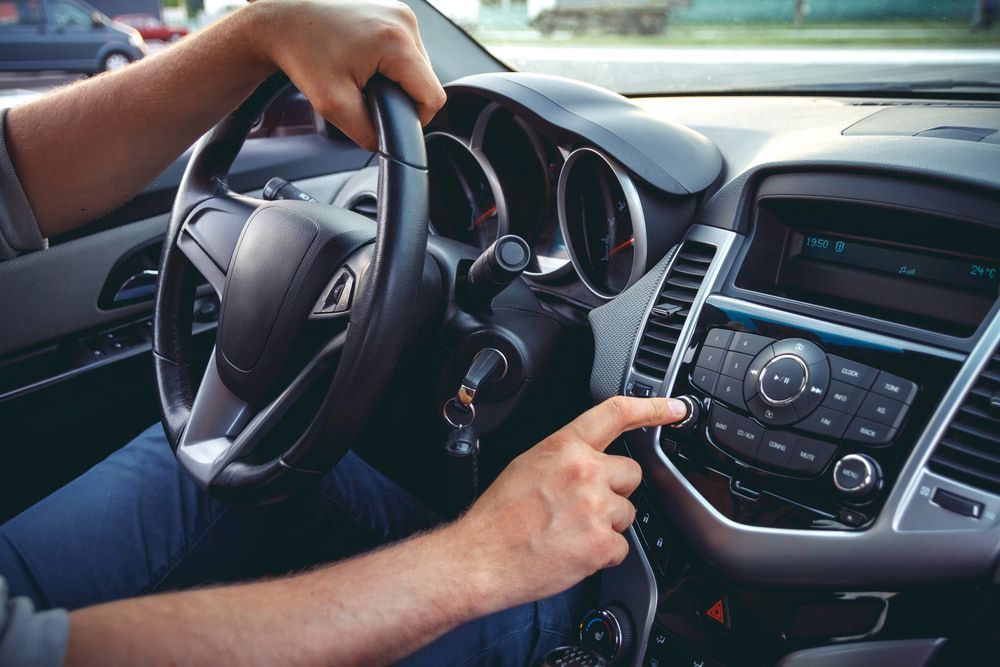 A Man Is Driving A Car And Pressing A Button On The Radio — Chris's Automotive & Marine Electrics In Darwin, NT