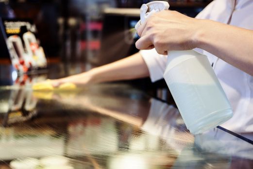 A Person Is Cleaning A Table With A Spray Bottle — Tailored Services in Rural View, QLD