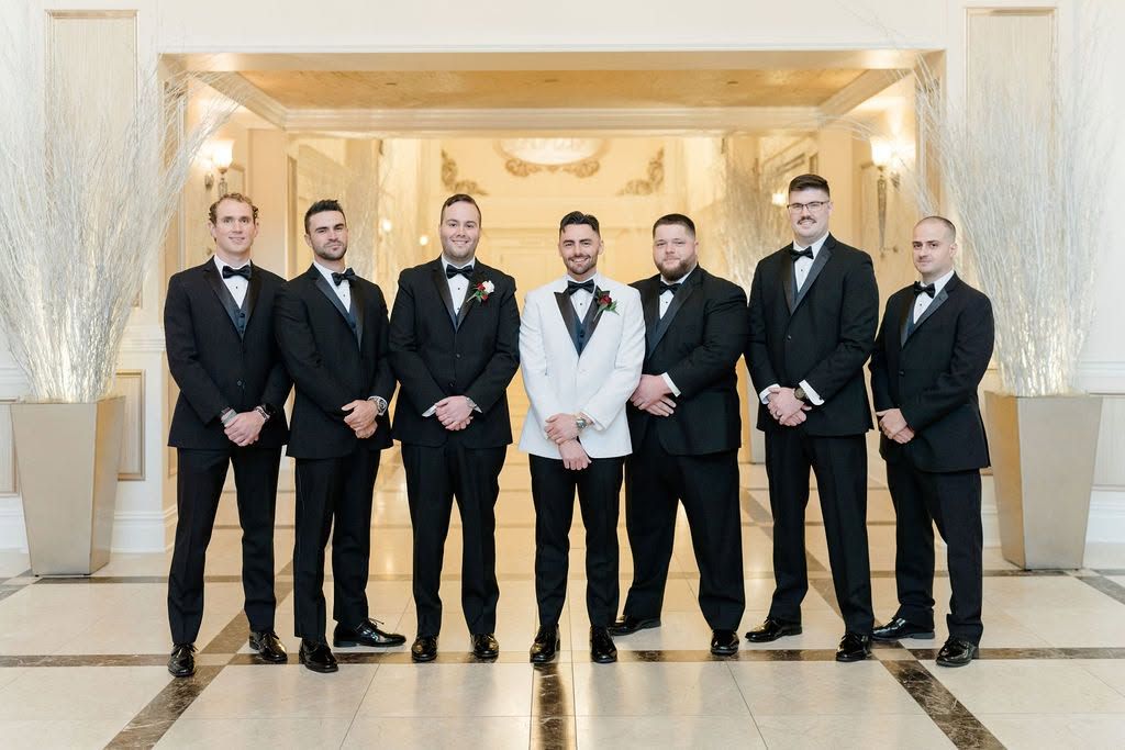Seven men in suits stand together in a bright lobby with gold decor.