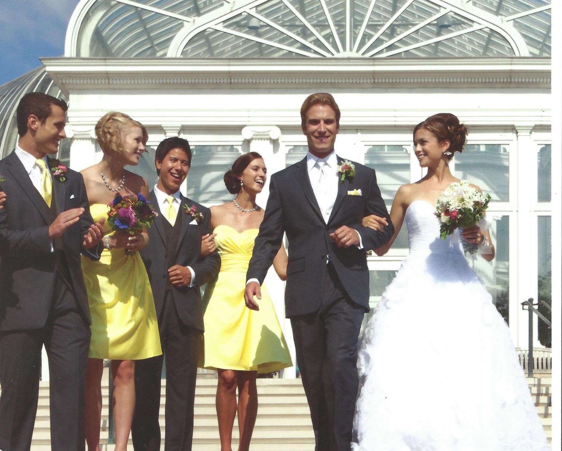 Wedding party walking outside a glass conservatory, with the bride in a white gown and groom in a black tuxedo