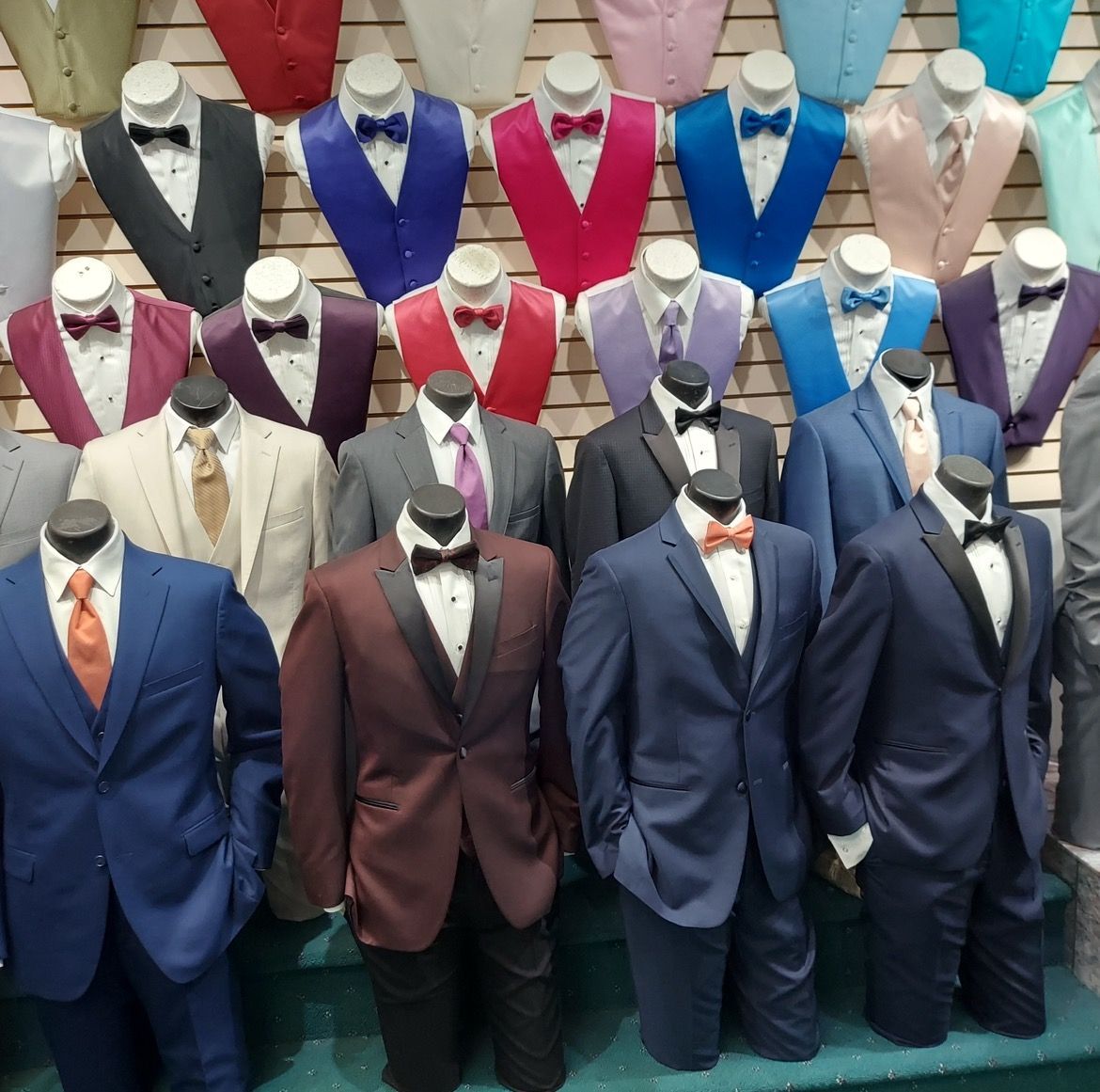 Mannequins in a clothing store display colorful men’s suits and ties arranged in rows.
