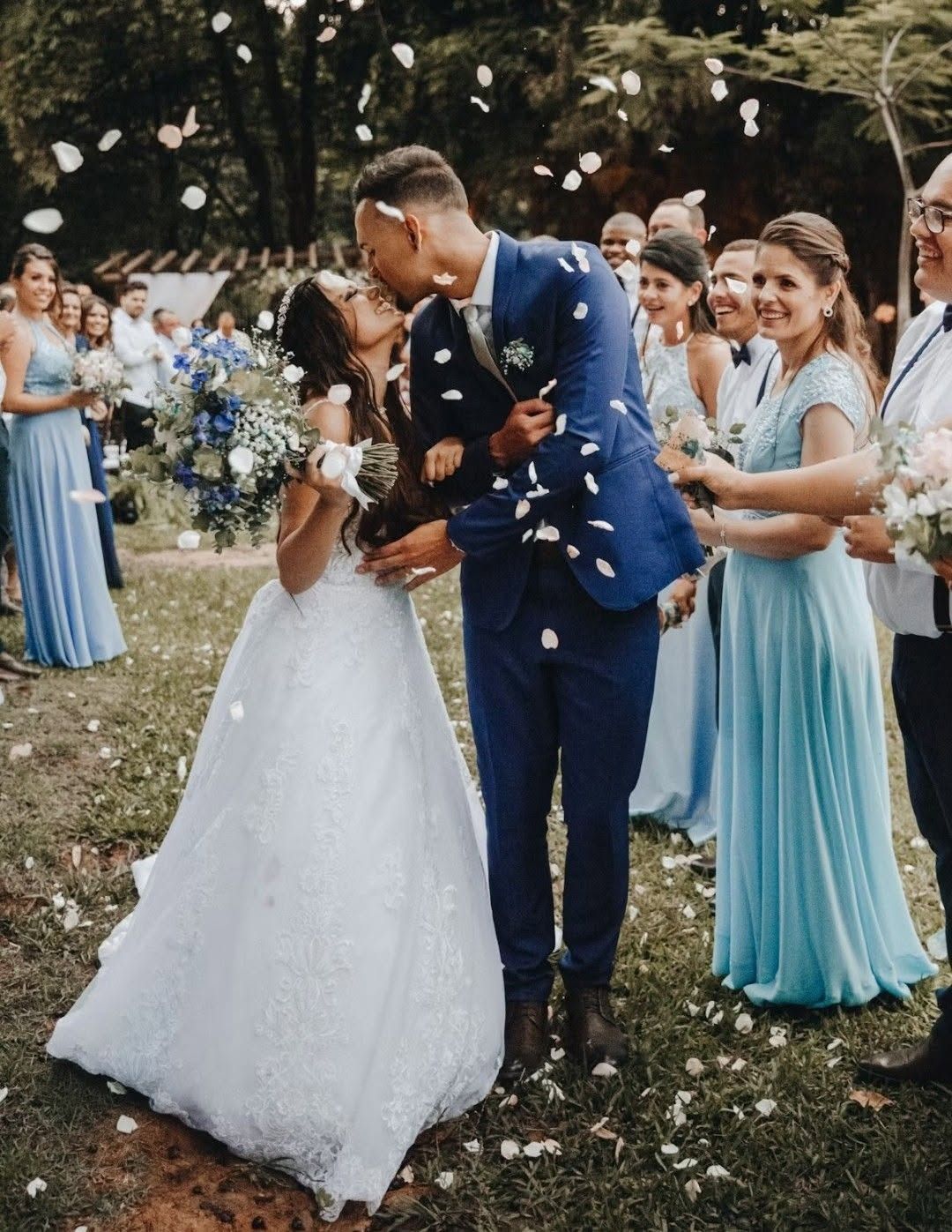 Bride and groom kissing at an outdoor wedding, bridesmaids in blue standing nearby