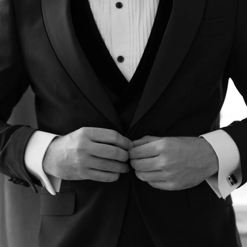 Person buttoning a black tuxedo jacket over a white dress shirt.