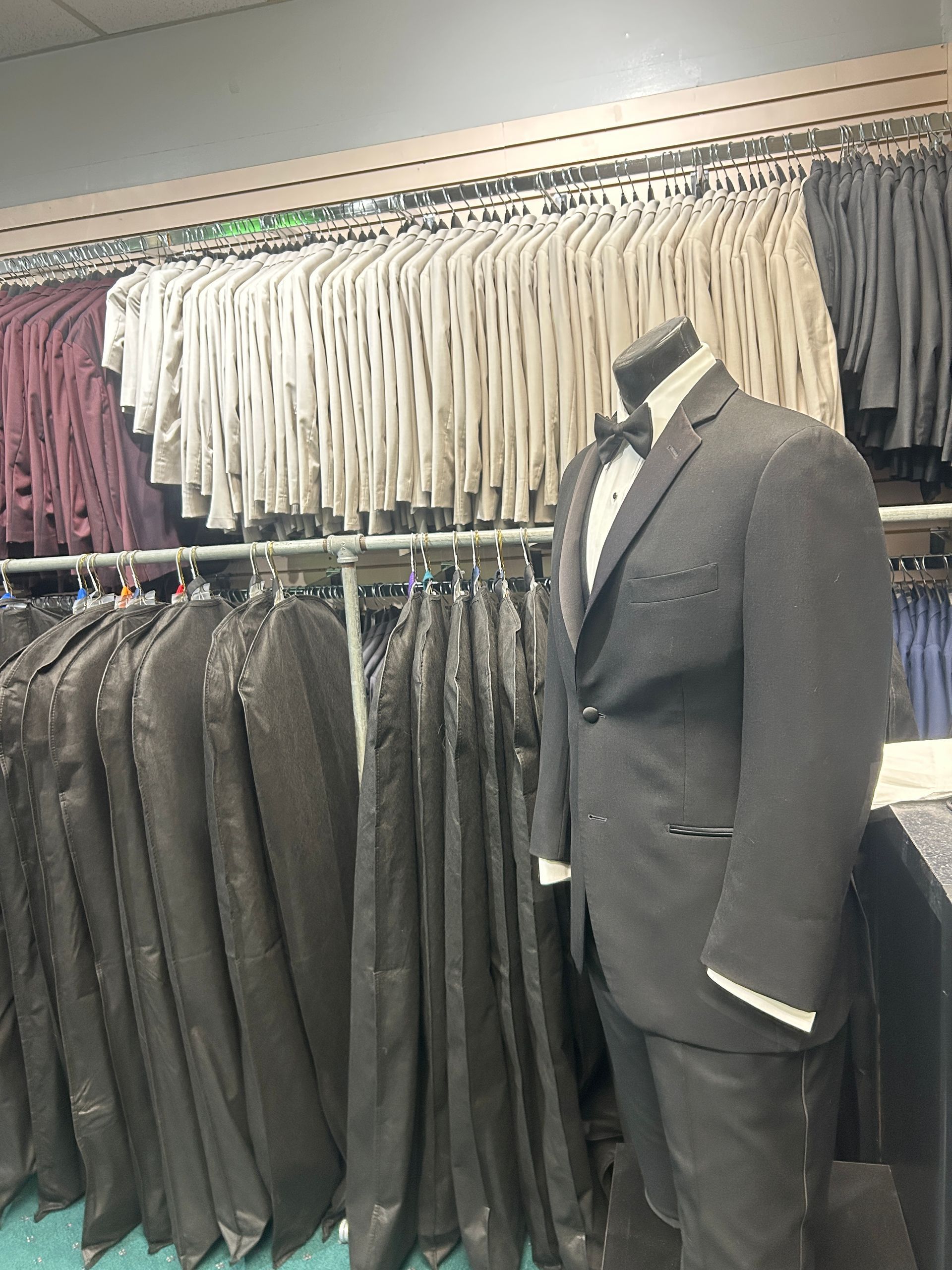 Suit displayed on mannequin in clothing store with rows of hanging jackets behind it