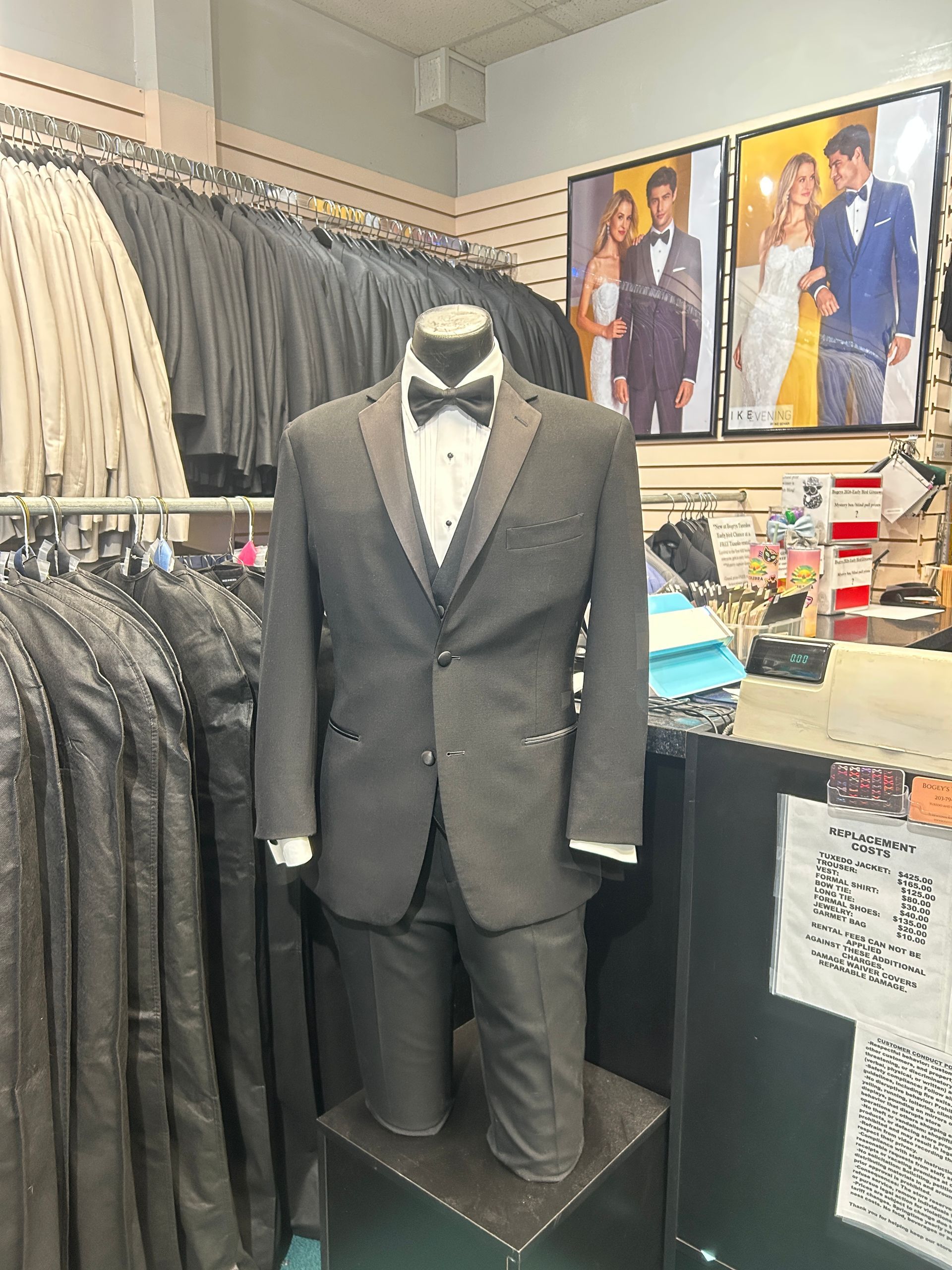 Mannequin in gray tuxedo suit displayed in a clothing store, surrounded by dress jackets and shirts.