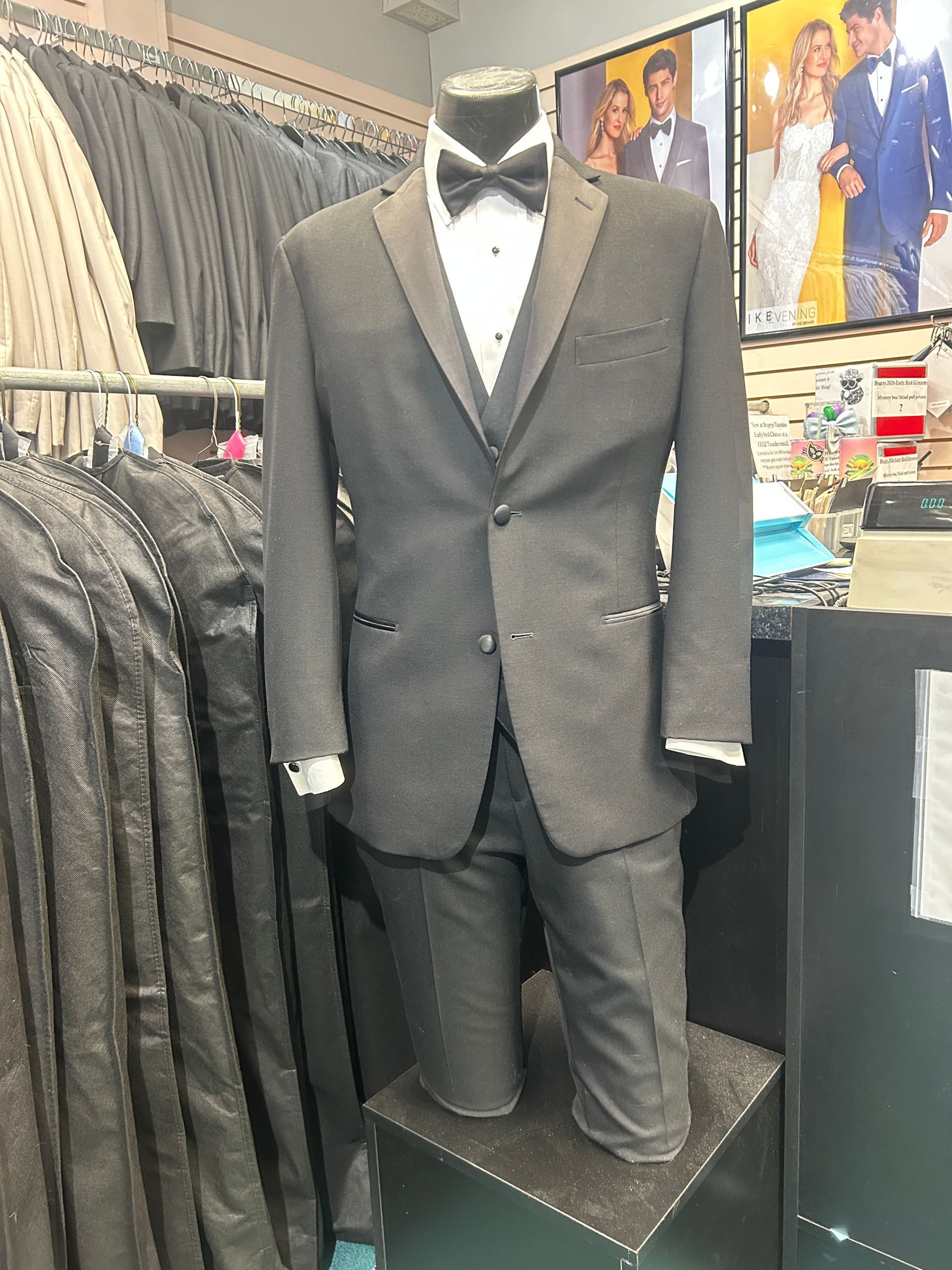 Black tuxedo on a mannequin in a menswear store, with shirts and suit posters in the background