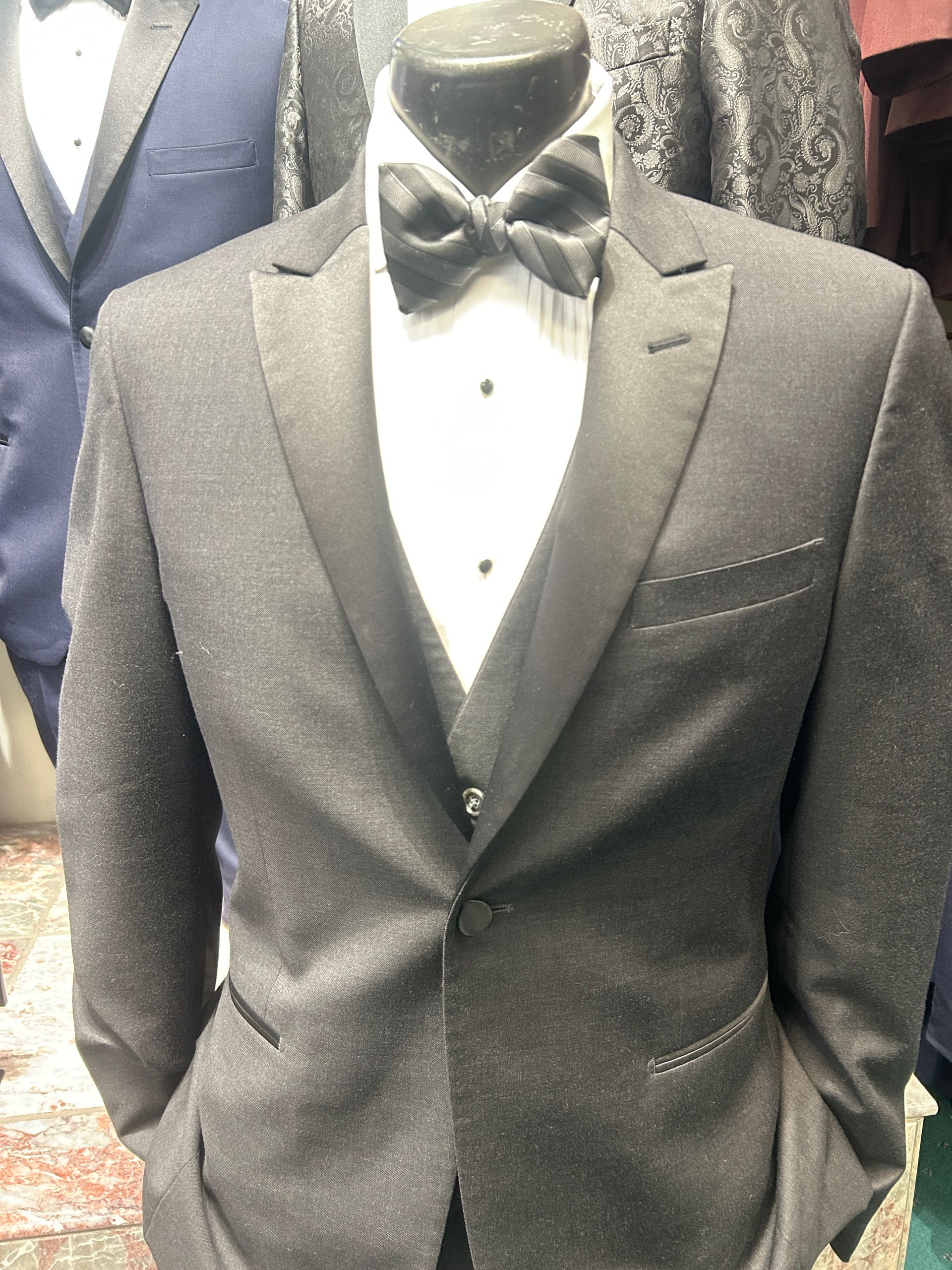 Black tuxedo jacket with white shirt and black bow tie on a mannequin.