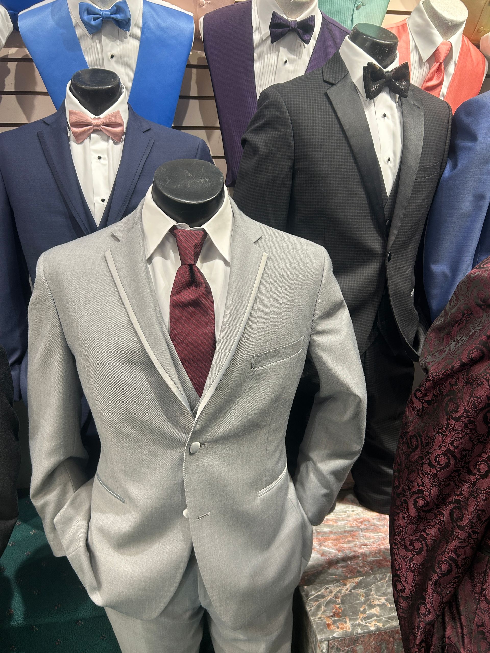 Suit jackets on mannequins in a clothing store, including gray, navy, and burgundy styles.