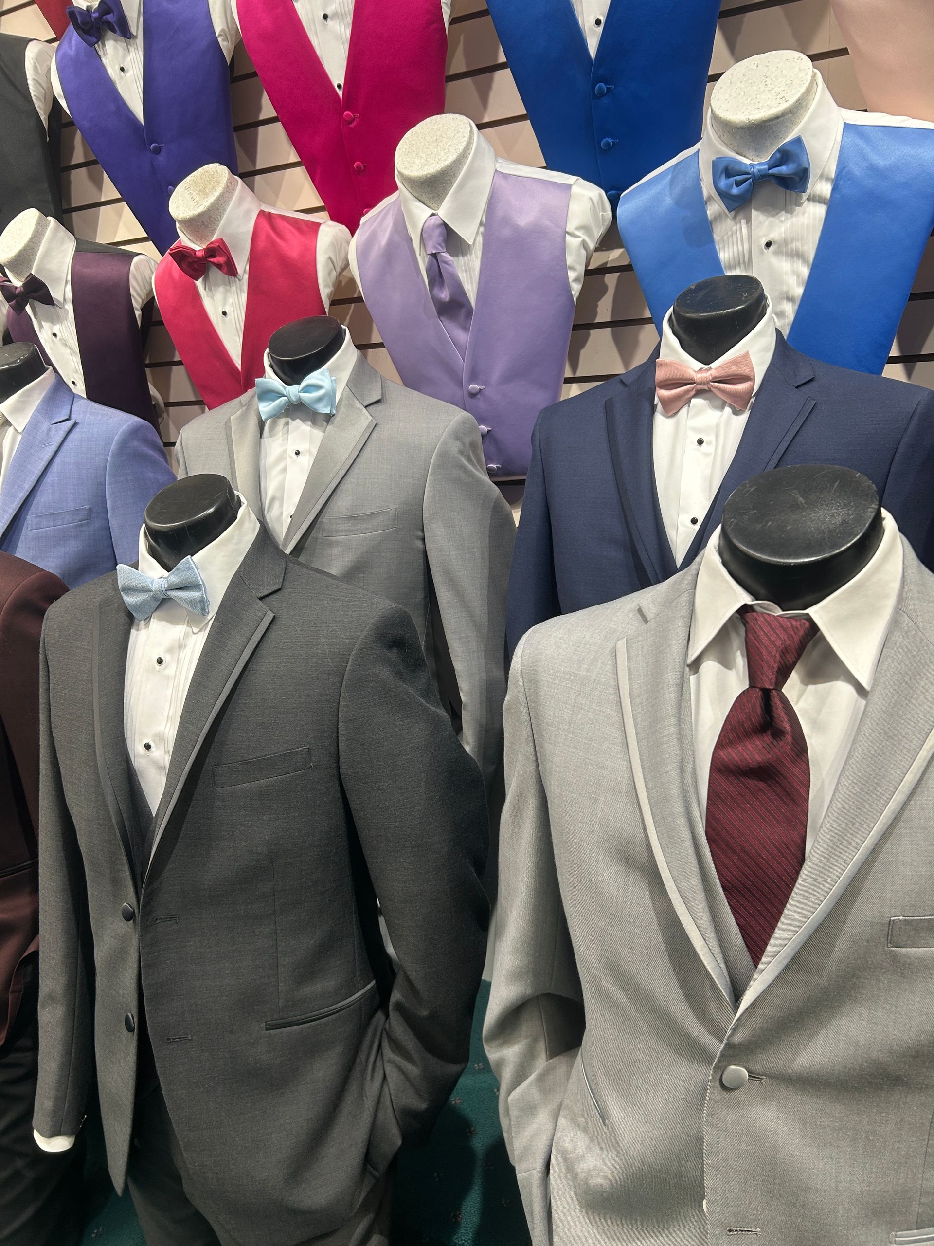 Mannequins in suits and ties displayed in a store, featuring gray, blue, purple, and burgundy jackets.