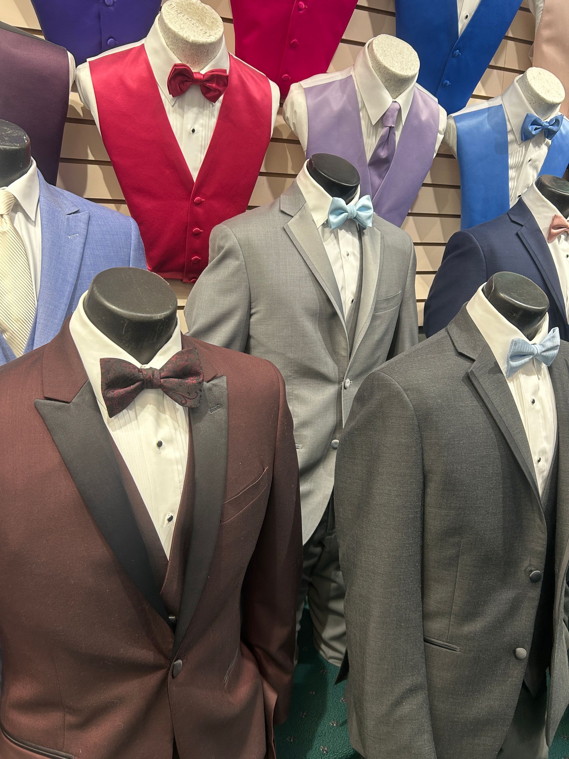 Mannequins in colorful tuxedos and suits displayed in a clothing store or showroom.