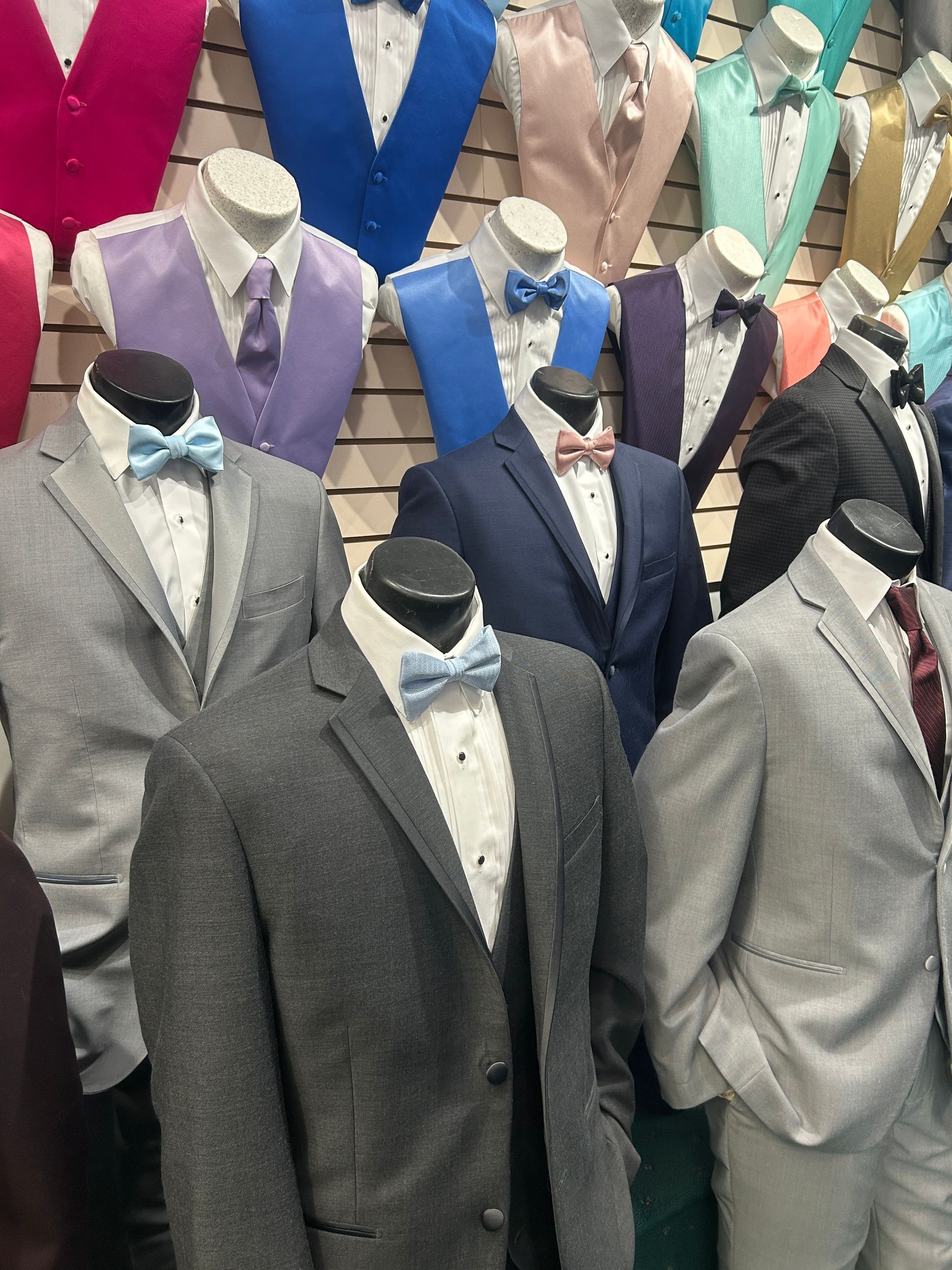 Mannequins in gray, navy, and black suits with bow ties displayed in a clothing store