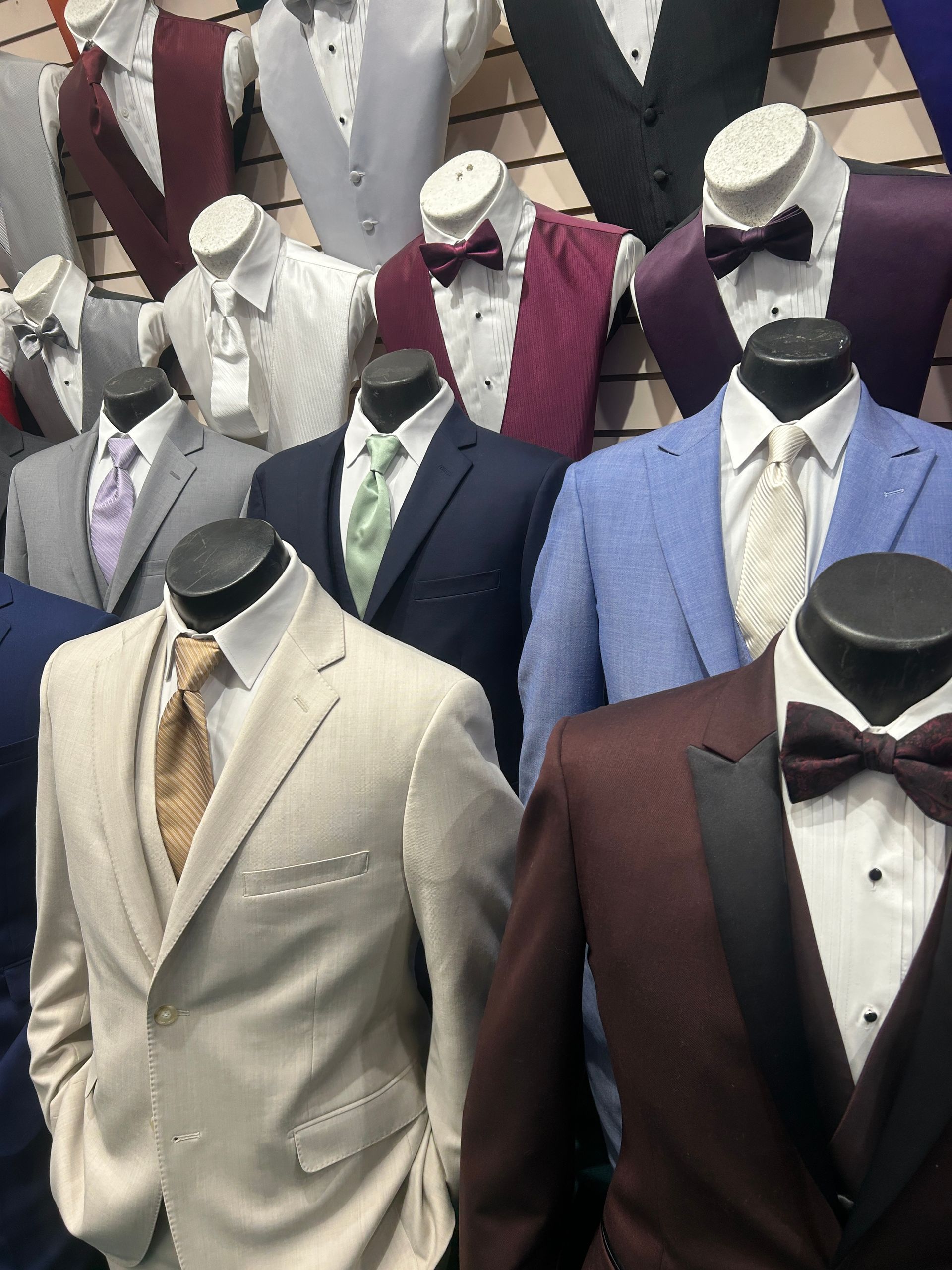 Mannequins wearing assorted suits and bow ties in a formalwear shop display.