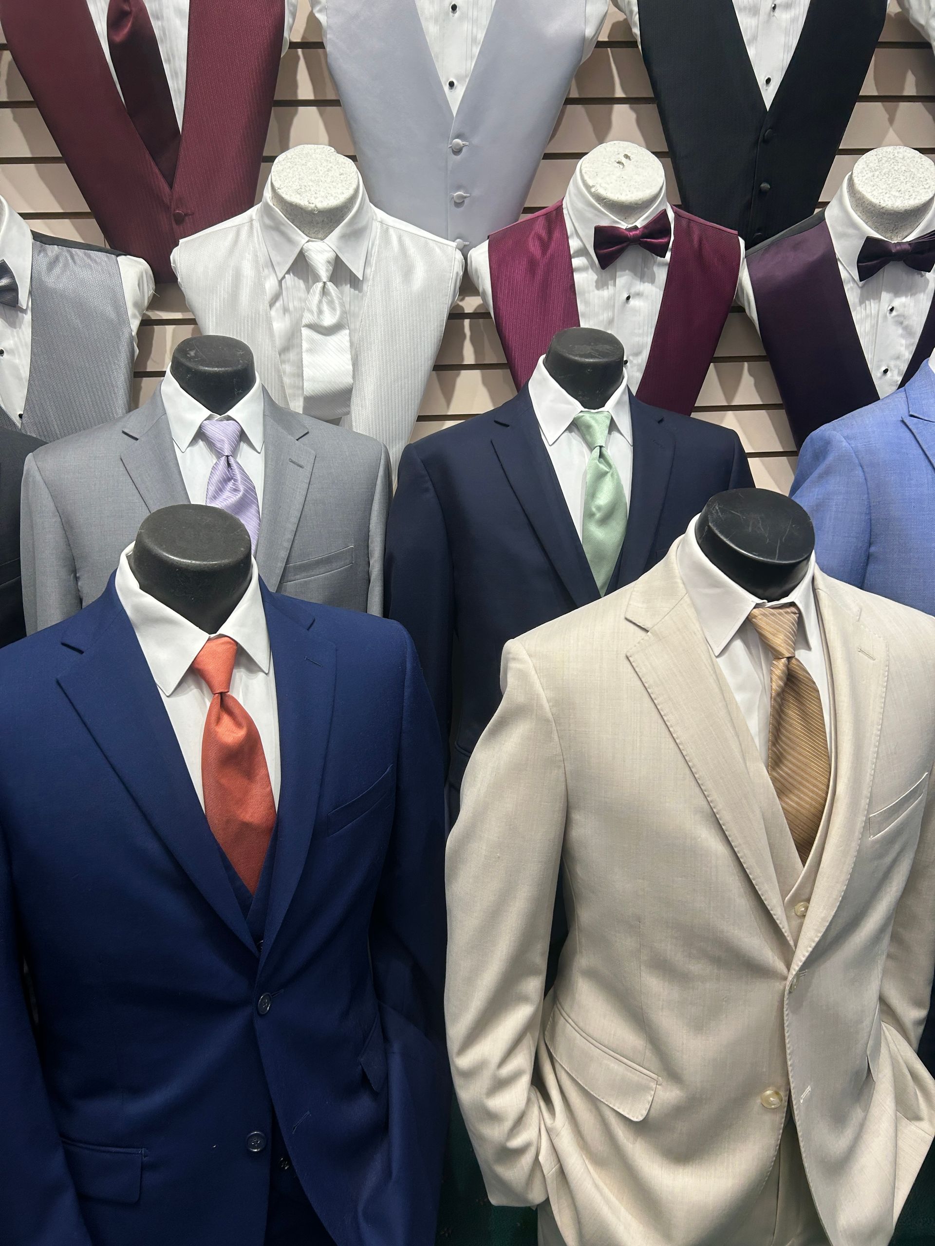 Mannequins displaying men’s suits in navy, beige, gray, white, and burgundy in a clothing shop