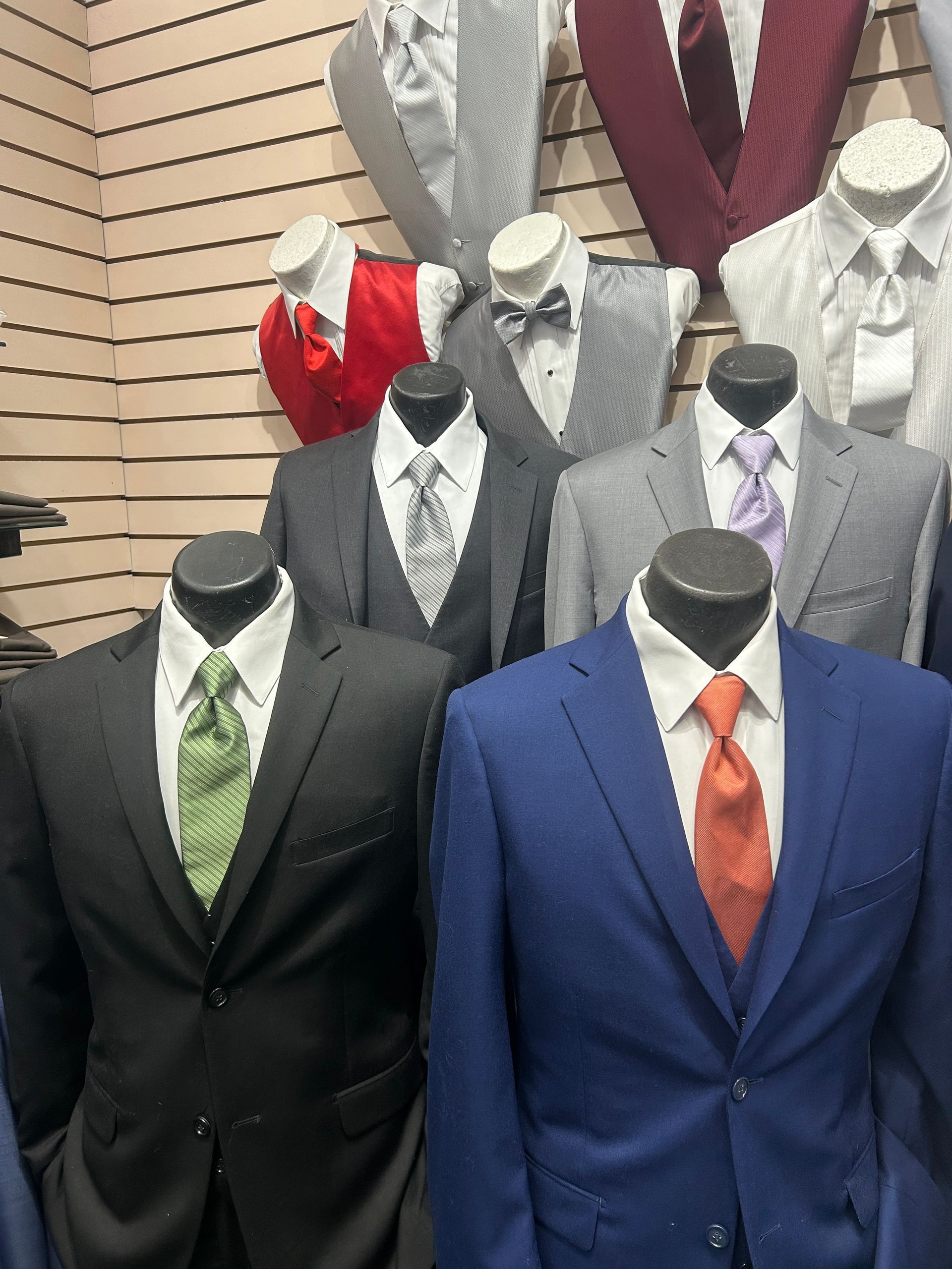 Mannequins in suits and ties displayed against a striped wall in a formalwear store.