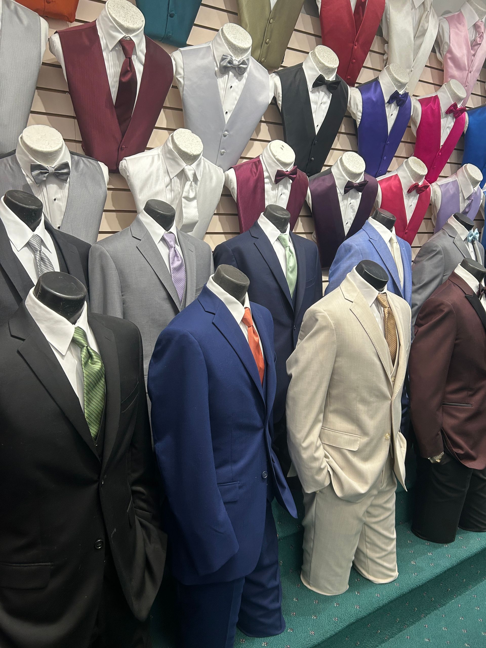 Mannequins in suits displayed in rows at a store, with assorted colors like black, blue, beige, and burgundy.