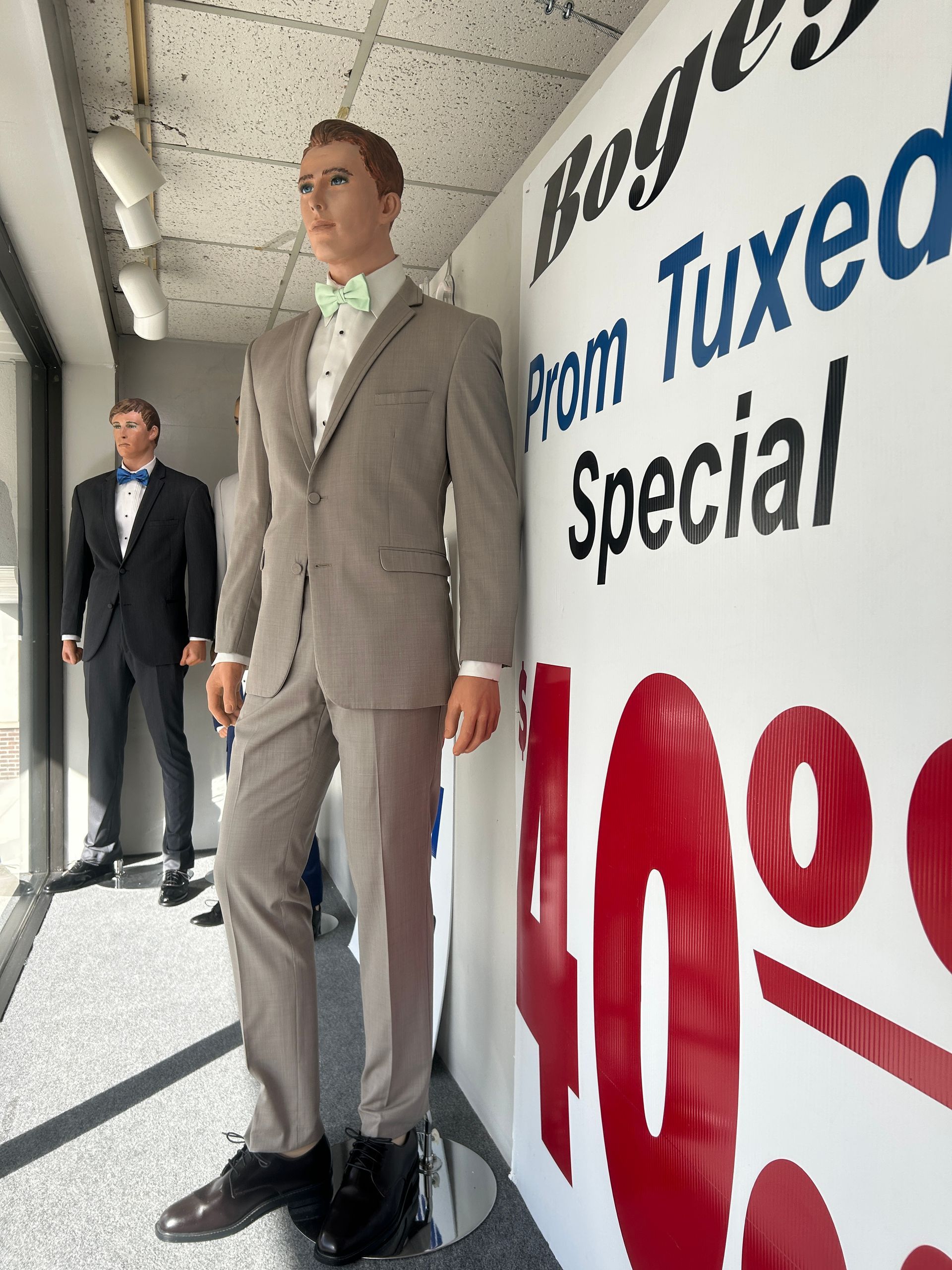 Two mannequins in tuxedos beside a store sign advertising tuxedo specials.