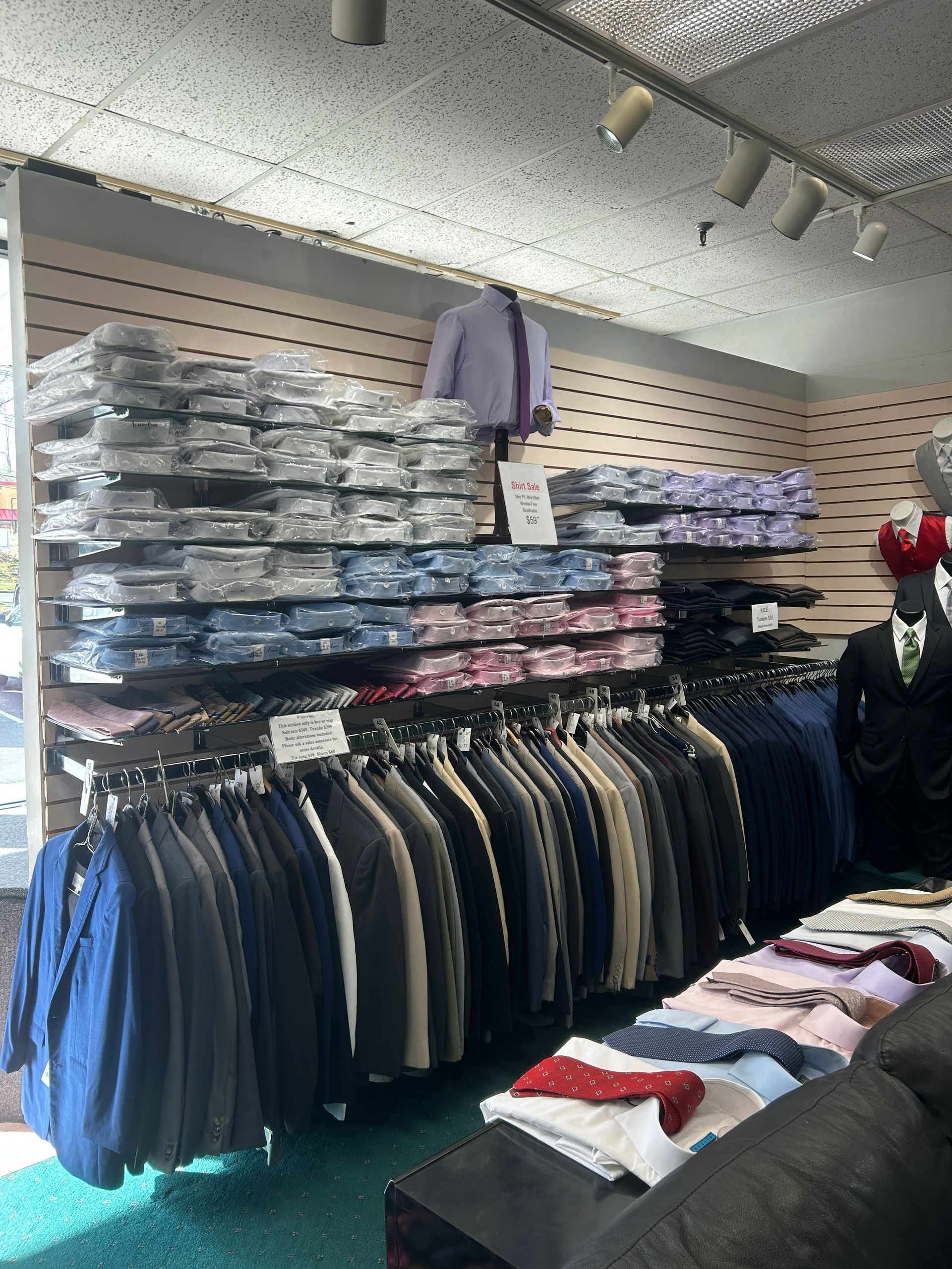 Clothing store display with folded shirts on shelves and hanging jackets, plus folded sweaters on a table.