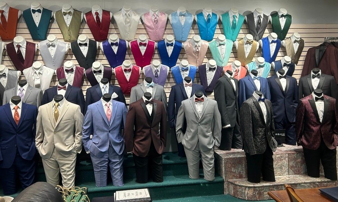 Mannequins in formal suits and ties displayed in a clothing shop window, with colorful suit jackets above.