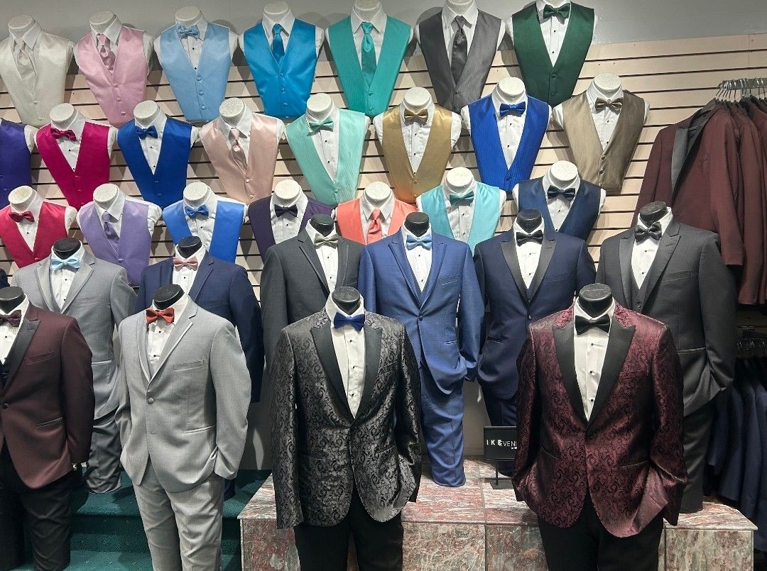 Mannequins display rows of colorful formal suits in a clothing store.