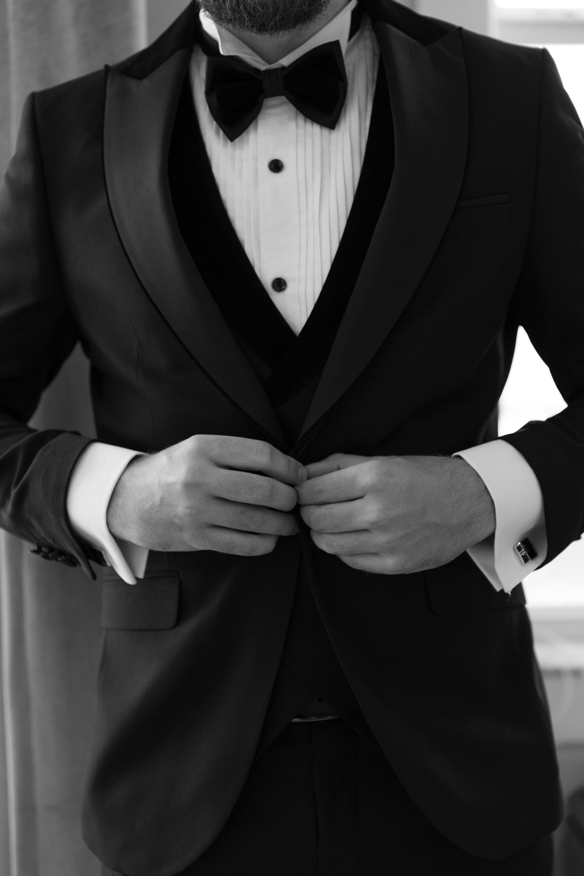 Person in a black tuxedo adjusting buttons on a white dress shirt
