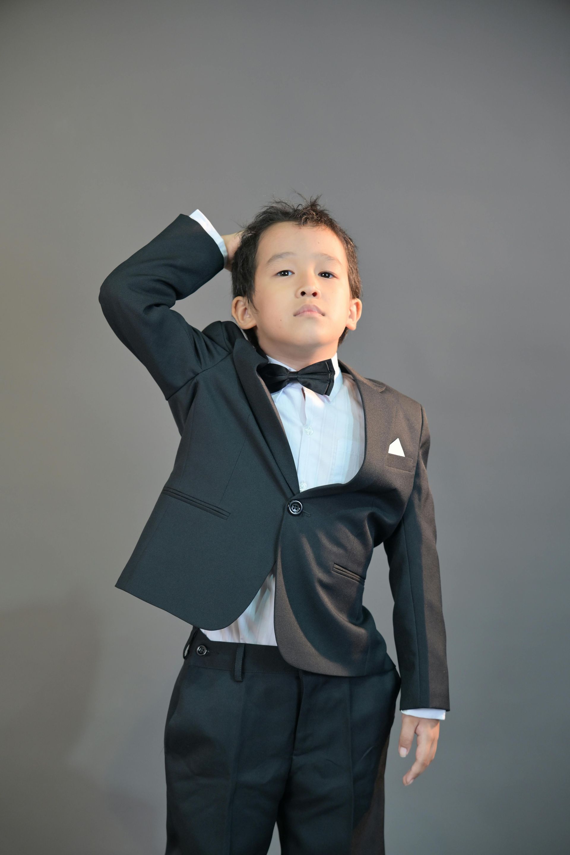 Young child in a dark suit and bow tie posing against a gray studio backdrop