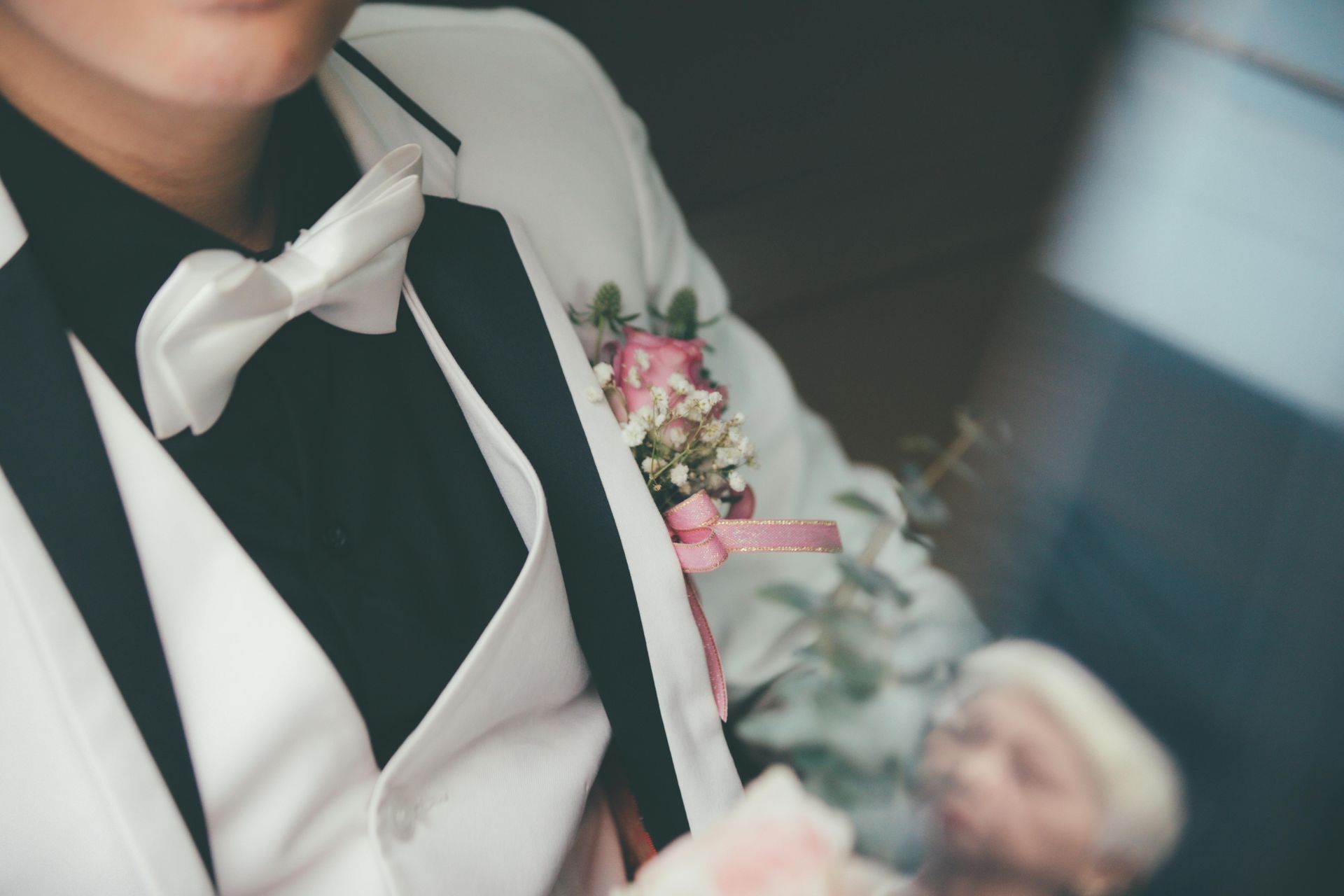 Person in a white tuxedo with black lapels and bow tie, holding a bouquet and bouquet flowers.