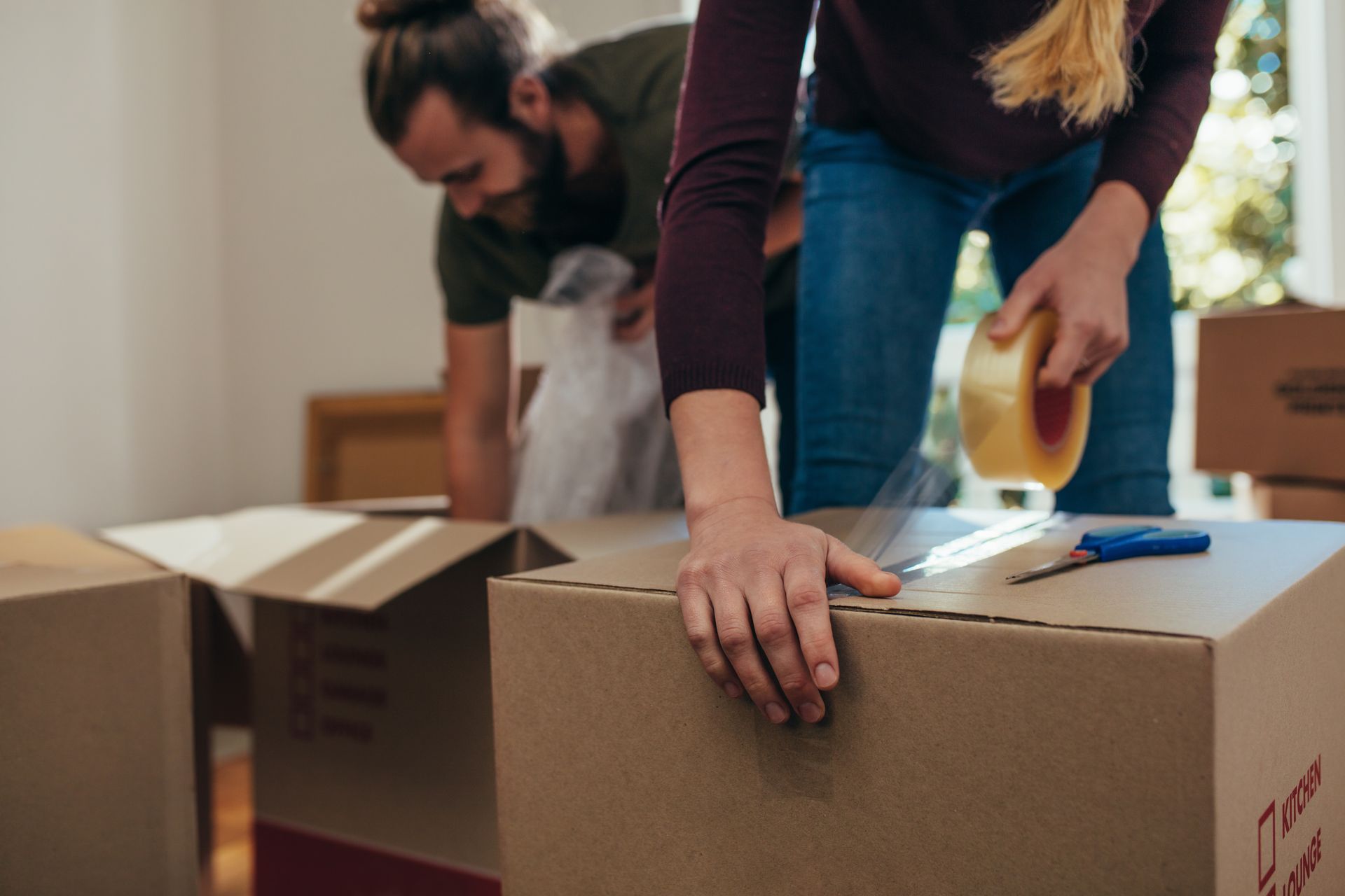 Man and woman packing cardboard moving boxes with tape and bubble wrap during home relocation.