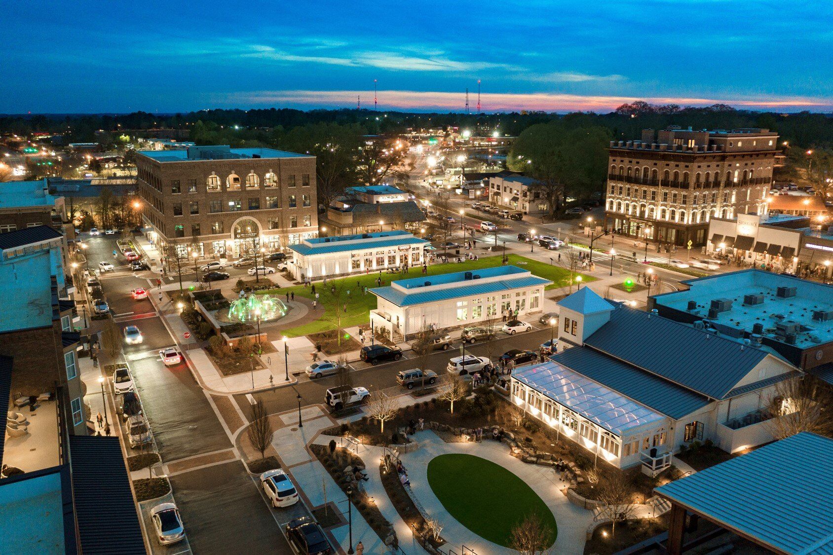 Aerial view of a bustling town square at dusk with lit buildings, streets, and blue-roofed market stalls