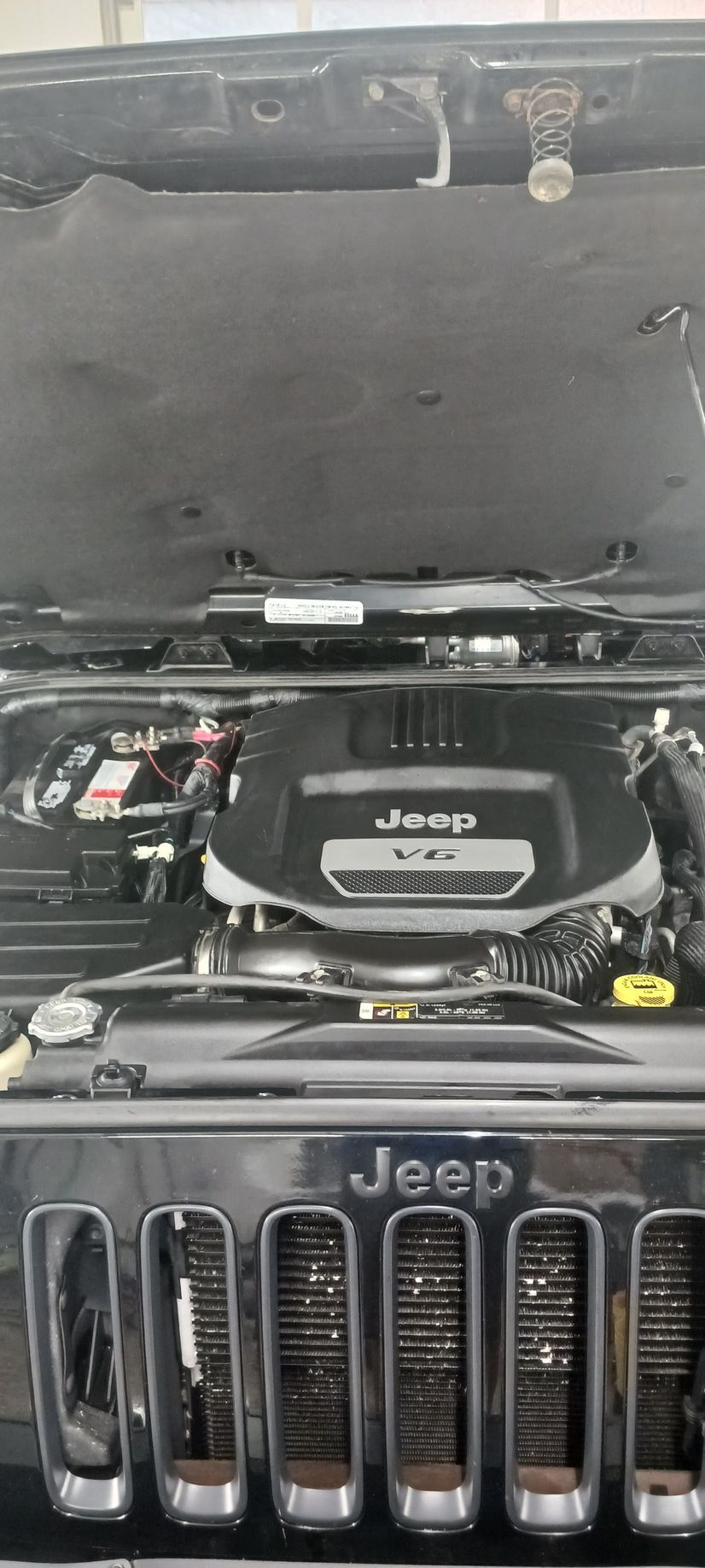 Jeep engine bay with hood open, showing the engine cover and front grille