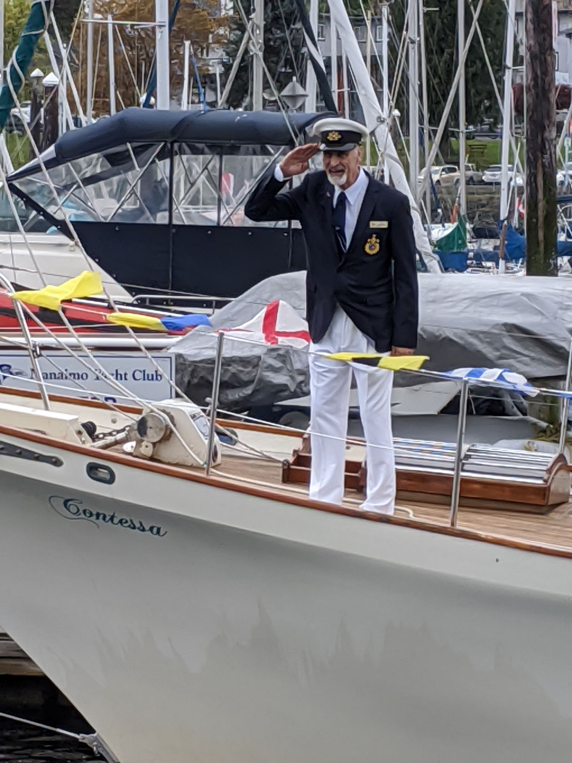 A man is saluting while standing on the deck of a boat.