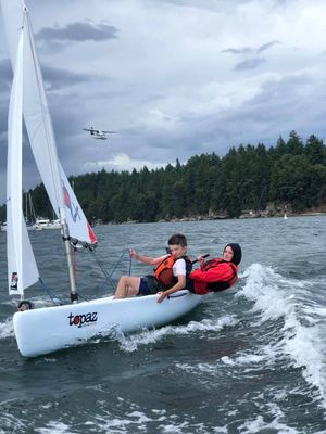 Two people are sailing a sailboat on a lake.