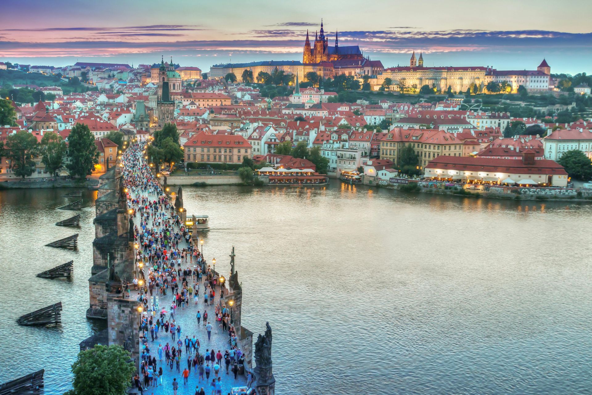 Charles Bridge in Prague, Czech Republic, crowded with people, overlooking a cityscape and illuminated castle.