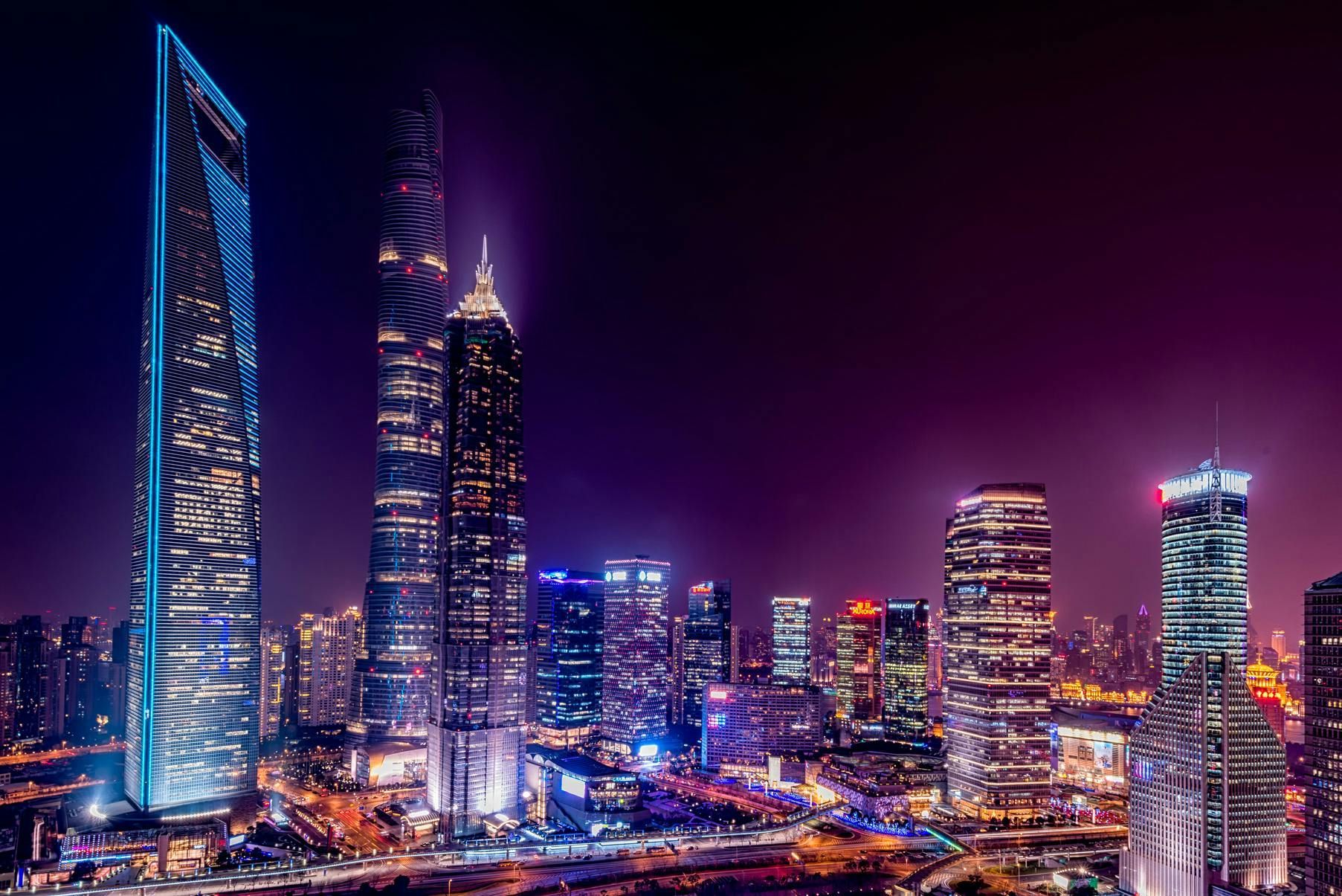 Nighttime cityscape of lit skyscrapers in shades of blue, purple, and yellow.