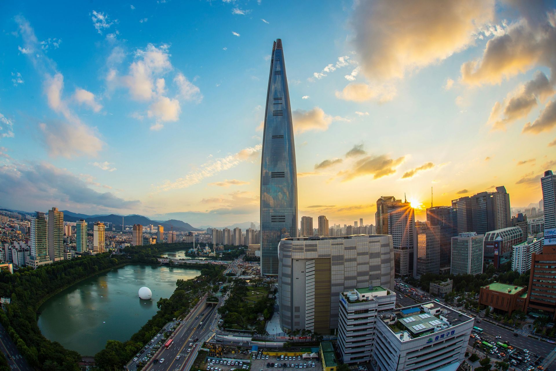 Lotte World Tower and Seoul skyline at sunset with a lake and city buildings.